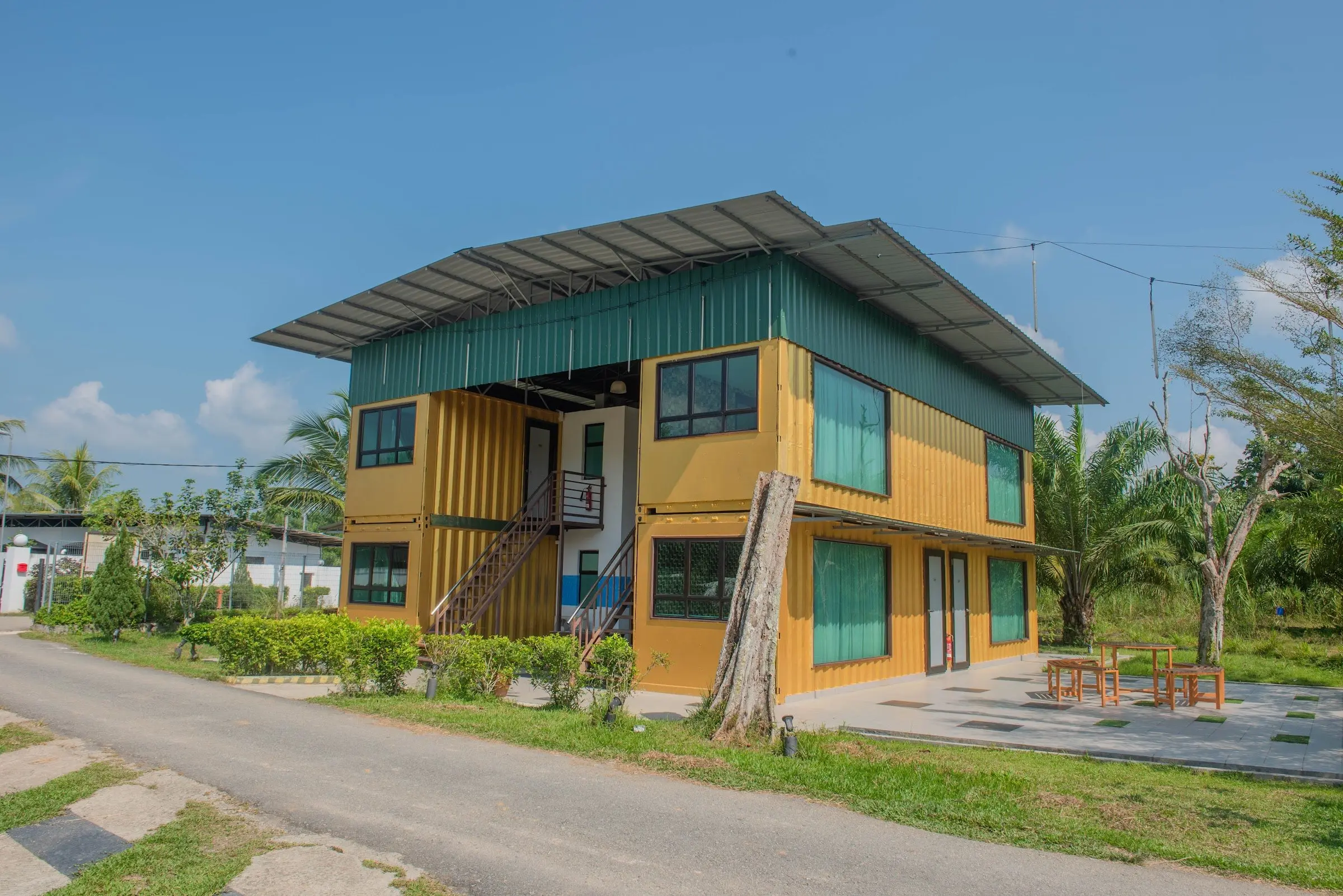 The upcycled shipping-container room block among palms and young trees