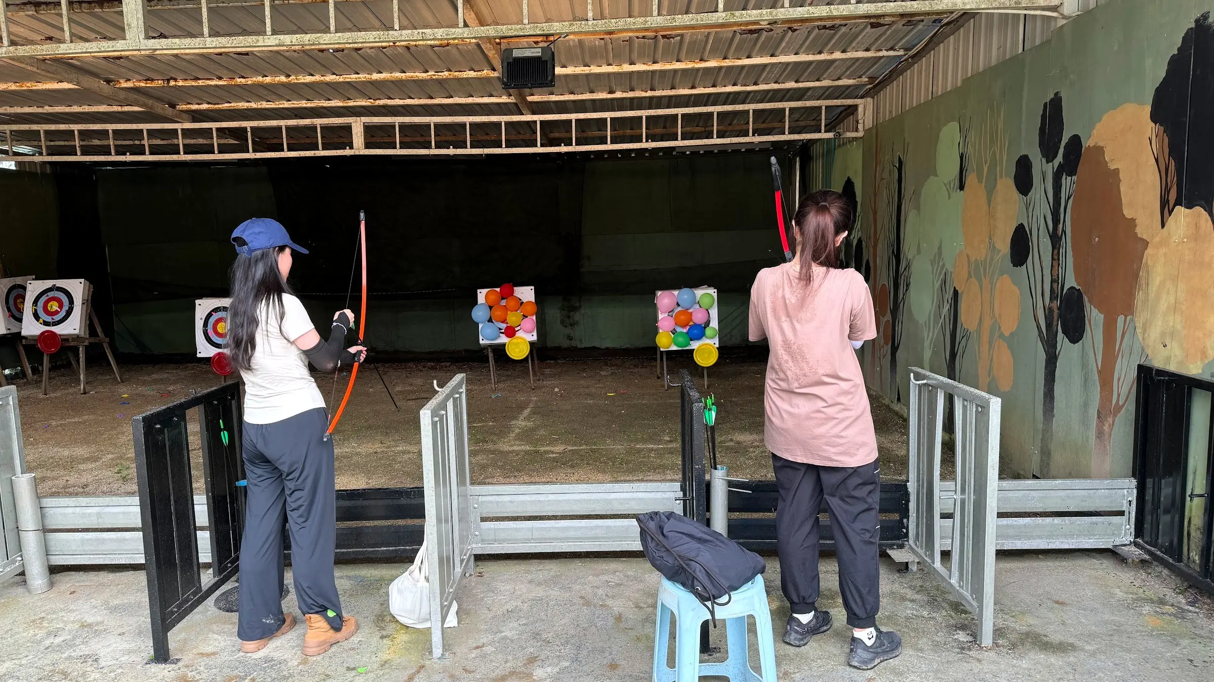 Two archers draw their bows at colourful targets in the covered Archery Range