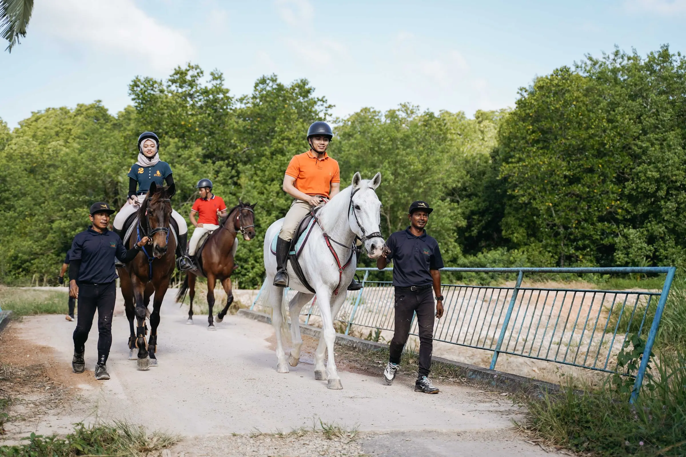 Guests ride horses along a leafy trail, led on foot by resort handlers