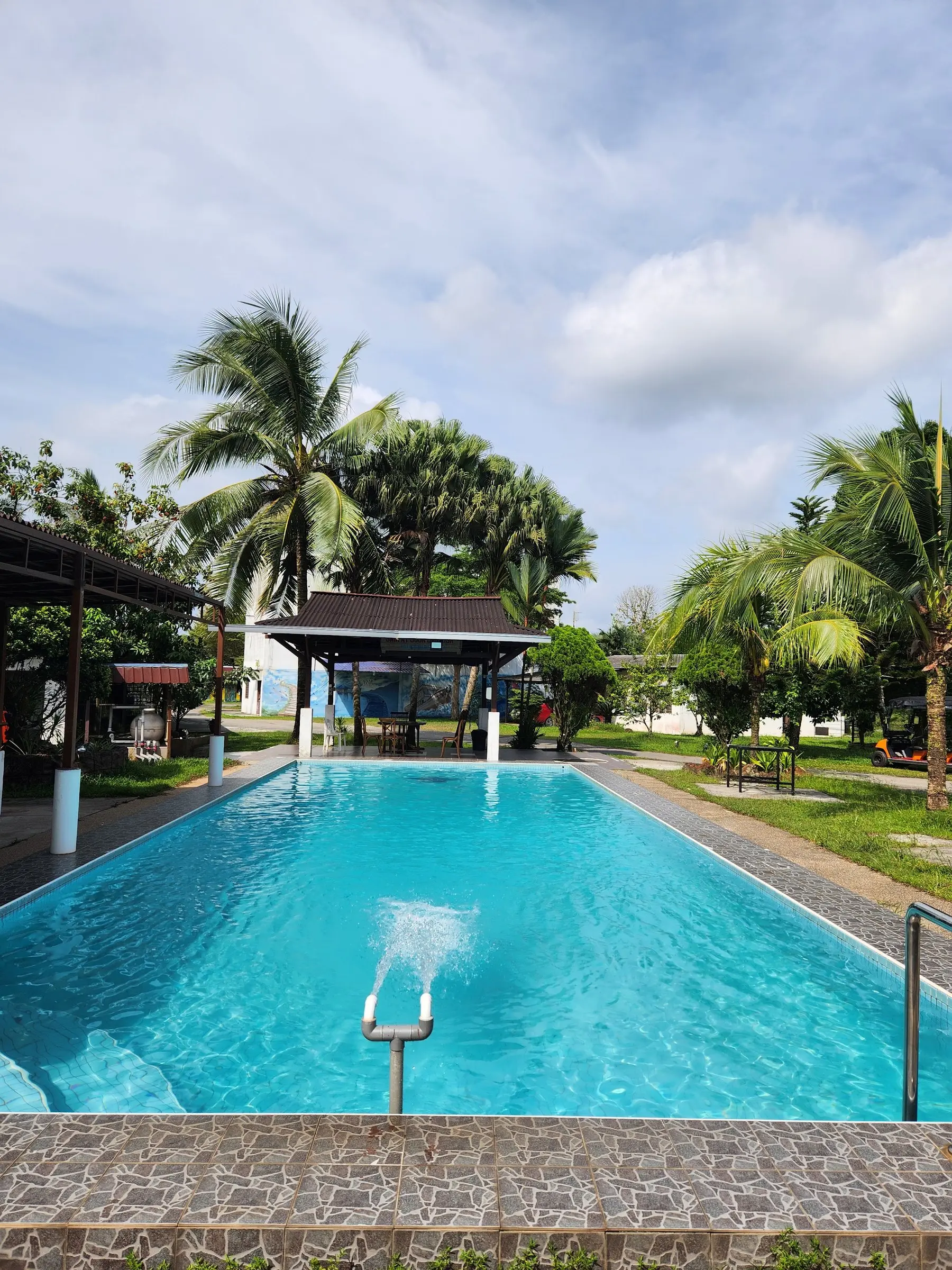 The blue Swimming Pool with fountain jets beside a thatched pavilion and palms