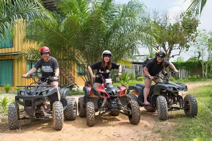 Three riders sit on muddy ATVs in front of the yellow container block
