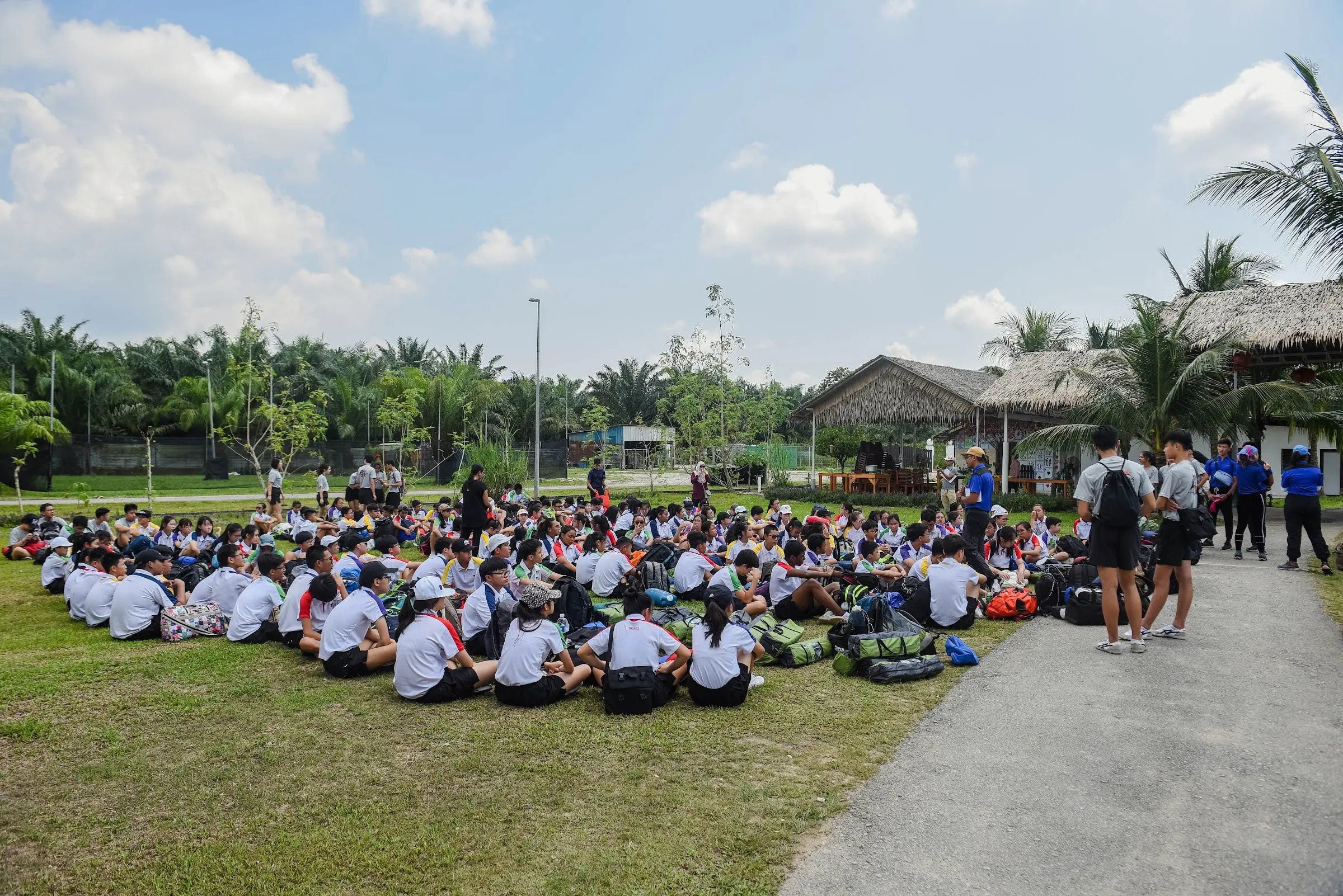 A large group sits together on the resort lawn under palm trees for a briefing