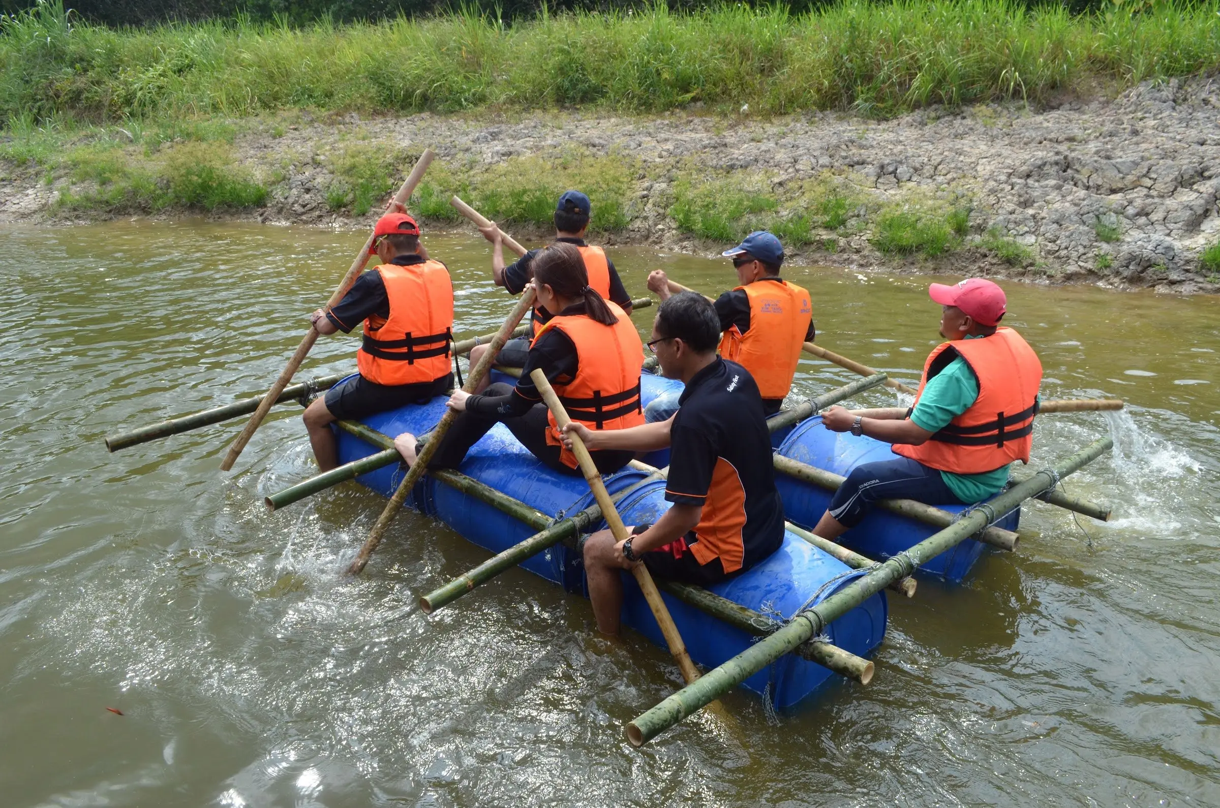 A team in orange life jackets paddles a home-built barrel-and-bamboo raft across the river