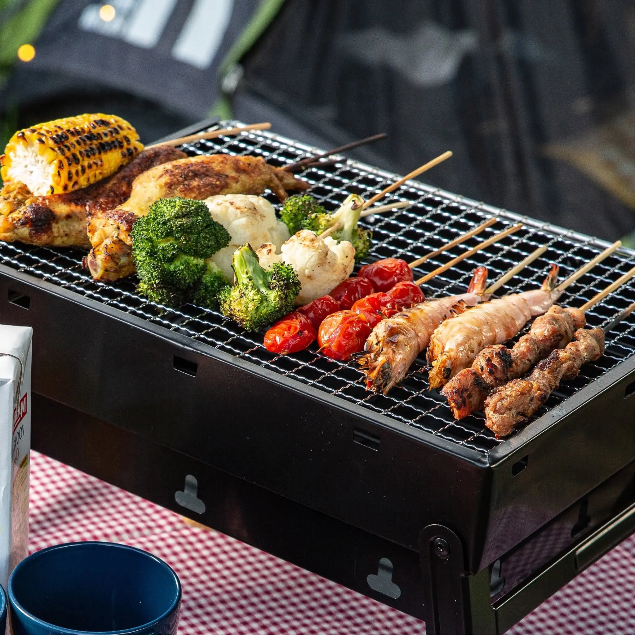 Chicken, corn, broccoli, tomatoes and skewers sizzling on a charcoal grill