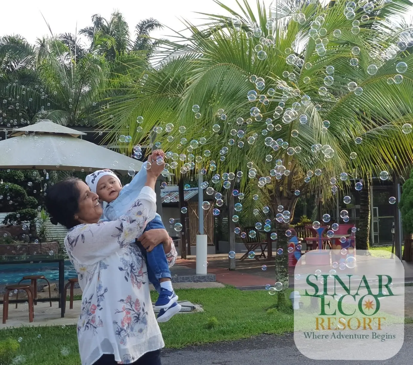 A grandmother lifts her grandson into a cloud of soap bubbles on the lawn by the Swimming Pool