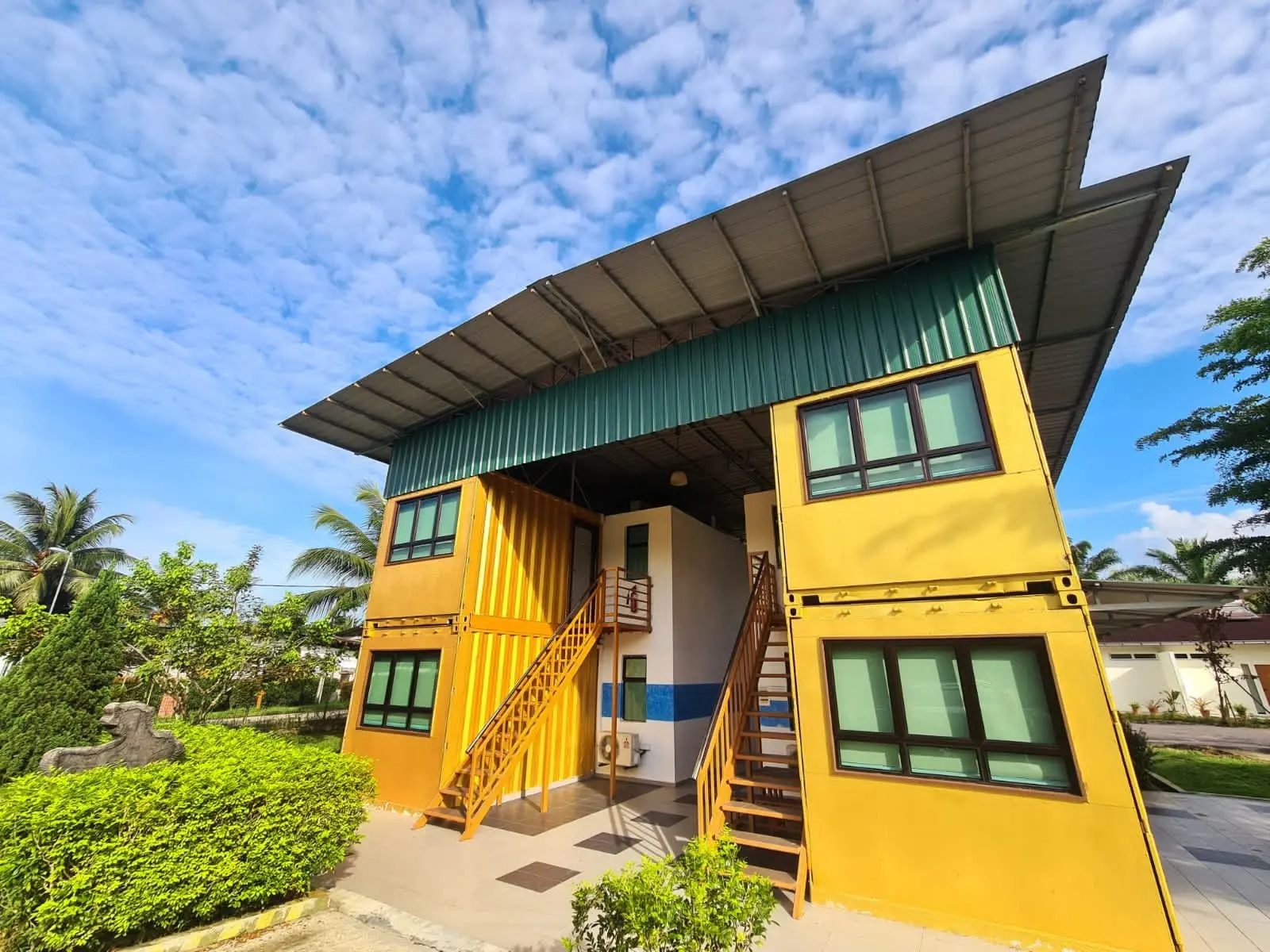 The yellow two-storey Container Room block under a blue, cloud-dotted sky