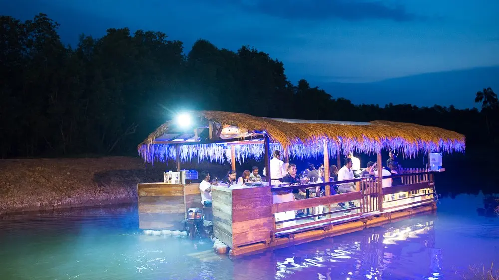 The thatched cruise raft lit up in blue at dusk on the dark river