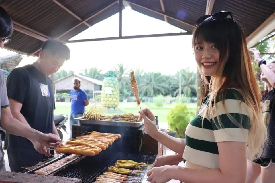 Guests grilling sausages and corn on an outdoor barbecue under the cafe roof