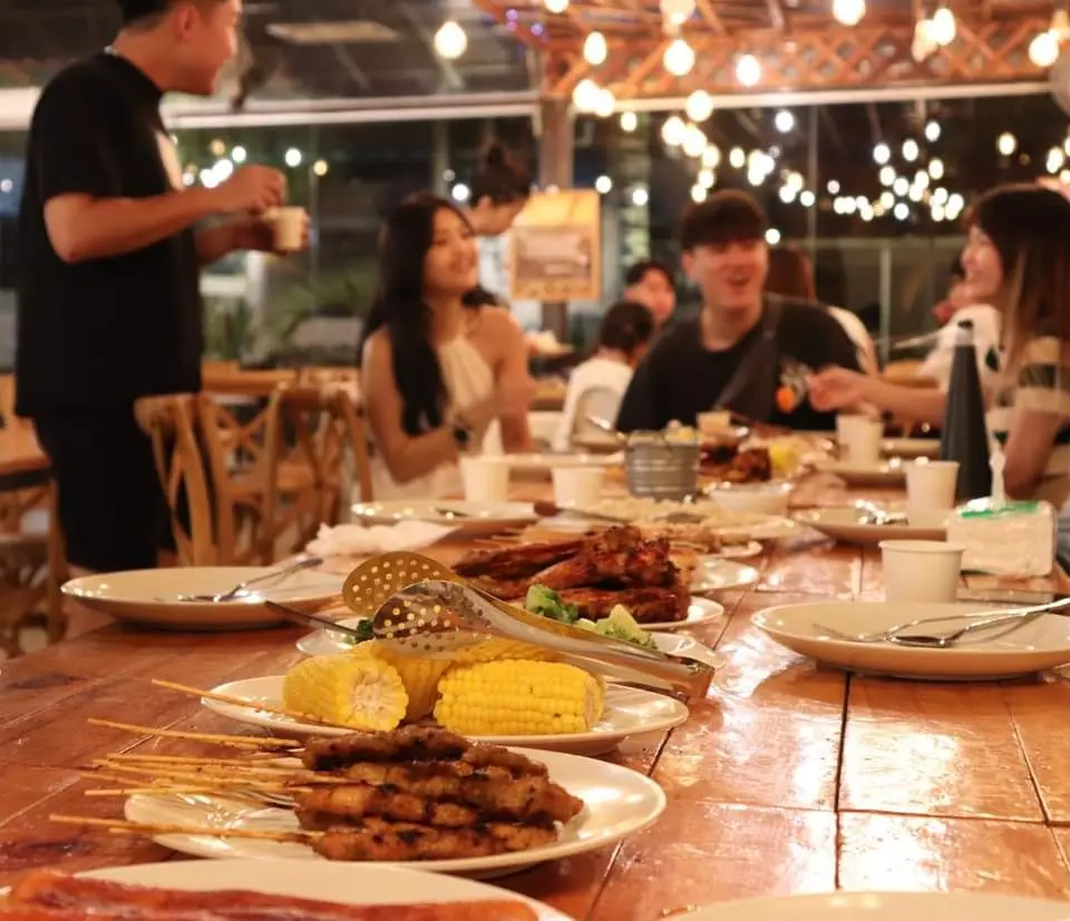 An evening BBQ Dinner of satay, grilled corn and chicken under strings of warm lights