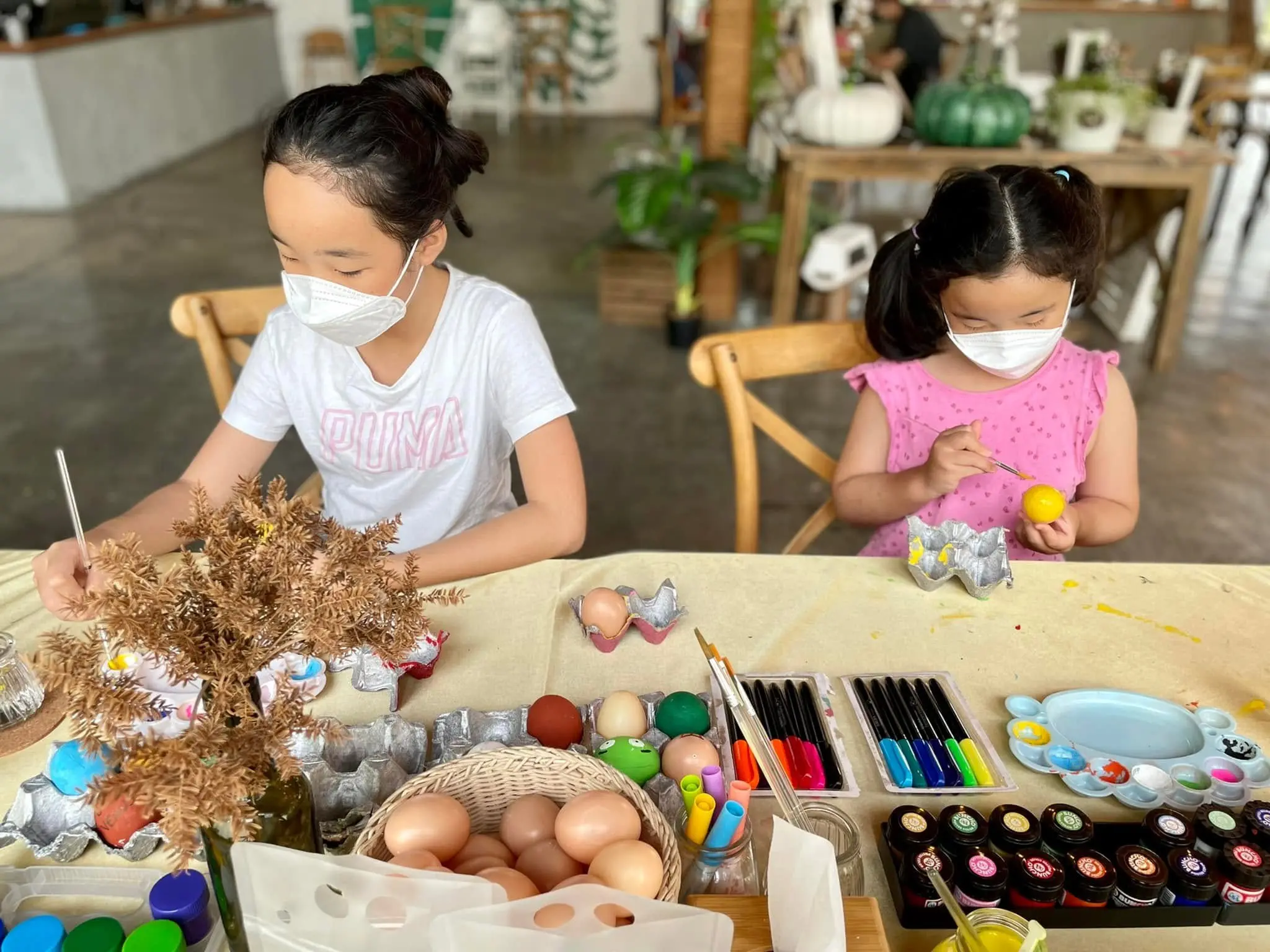 Two girls paint eggs at a craft table during a Special Workshop at the cafe