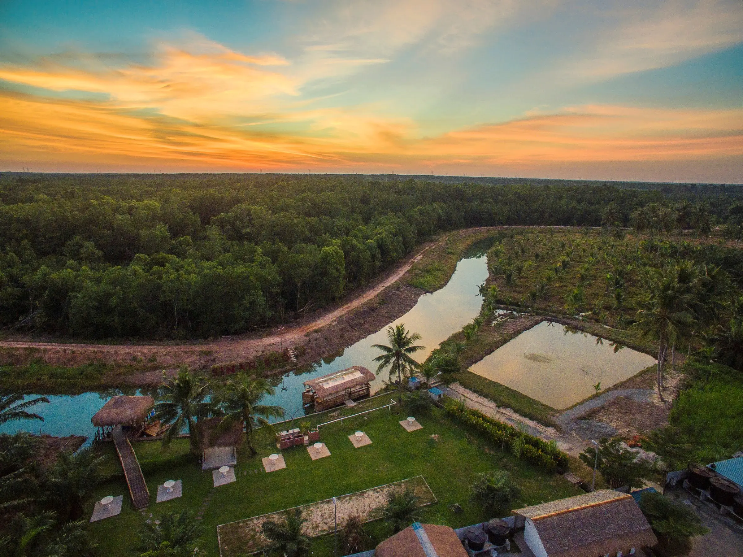 Golden-hour aerial view of Sinar Eco Resort, its lake and river inside the oil palm estate