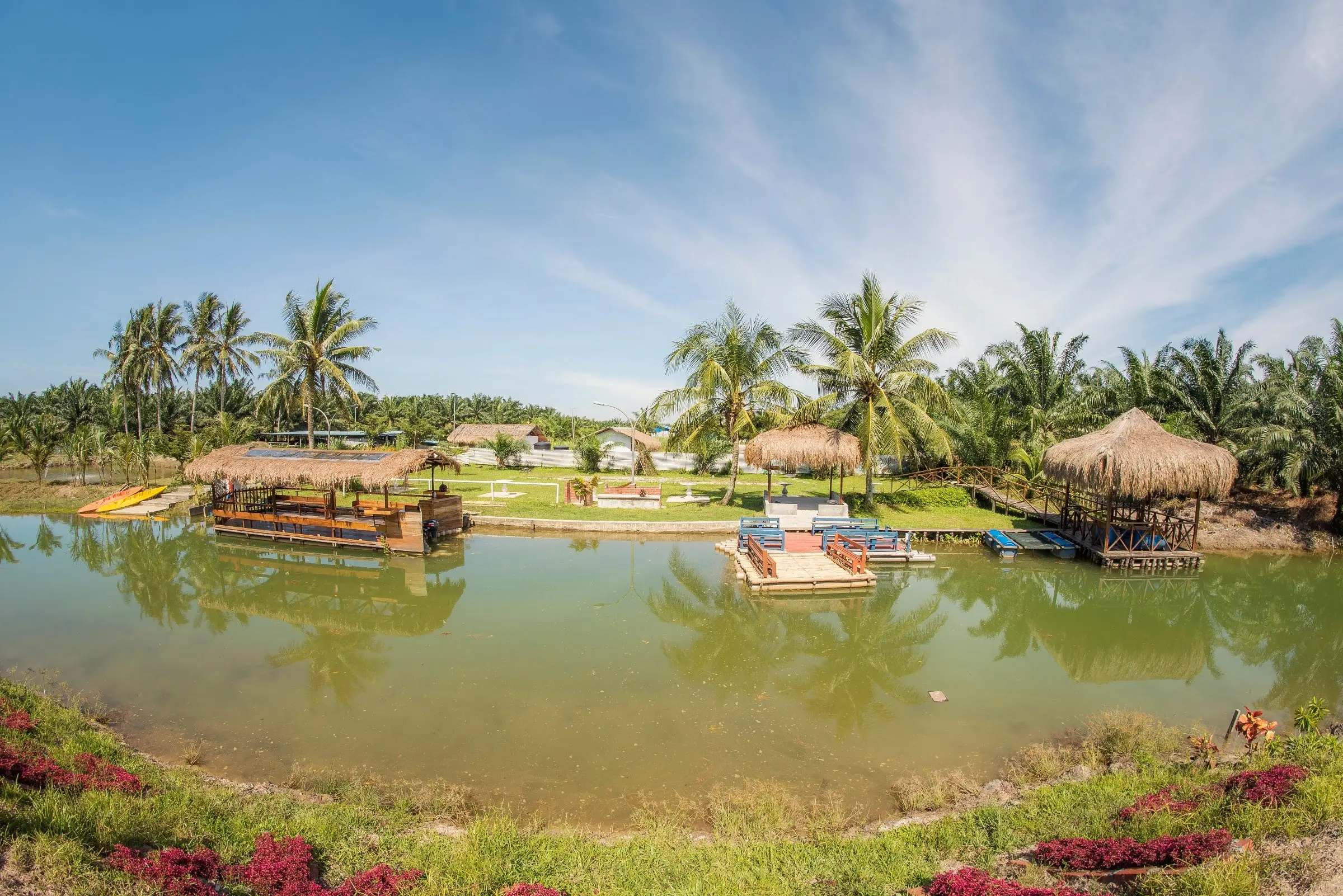Thatched gazebos and floating platforms around a calm lake lined with coconut palms