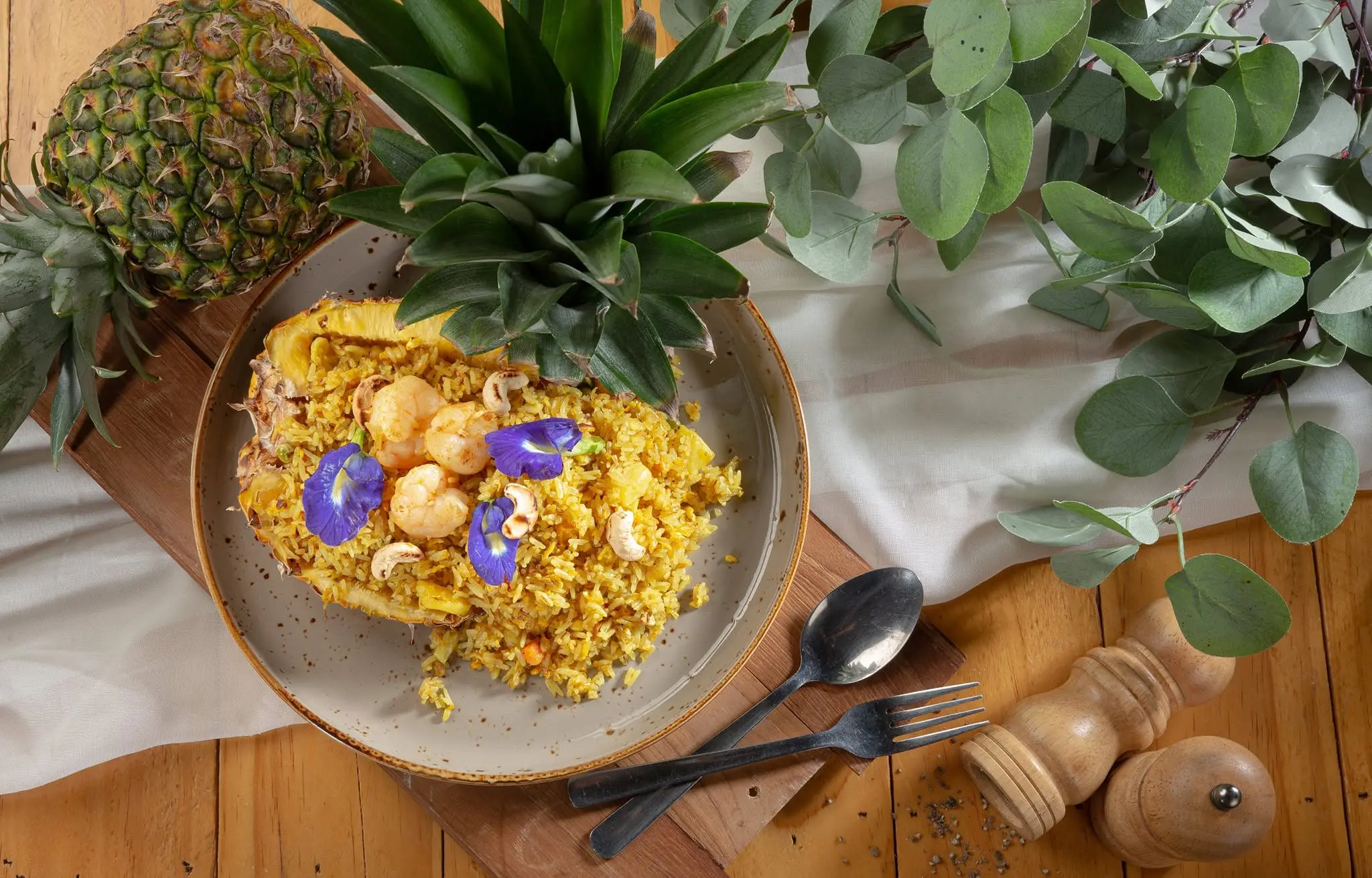Pineapple fried rice with butterfly pea flowers, served beside a fresh pineapple