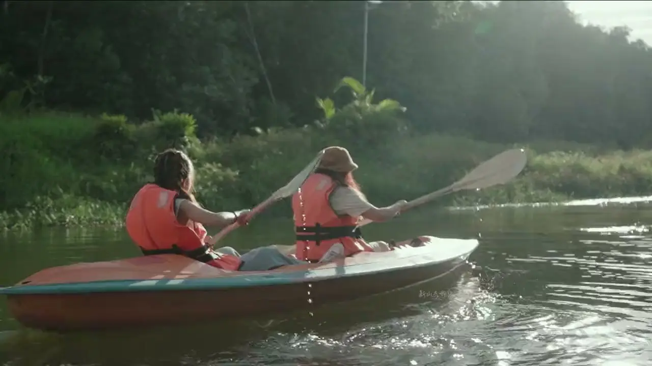 Two kayakers in life jackets paddle a tandem kayak on a backlit jungle river