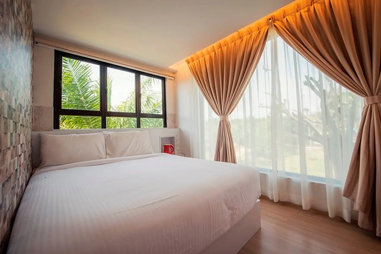 Container Room queen bed in warm cove light beside a wide window and drawn curtains