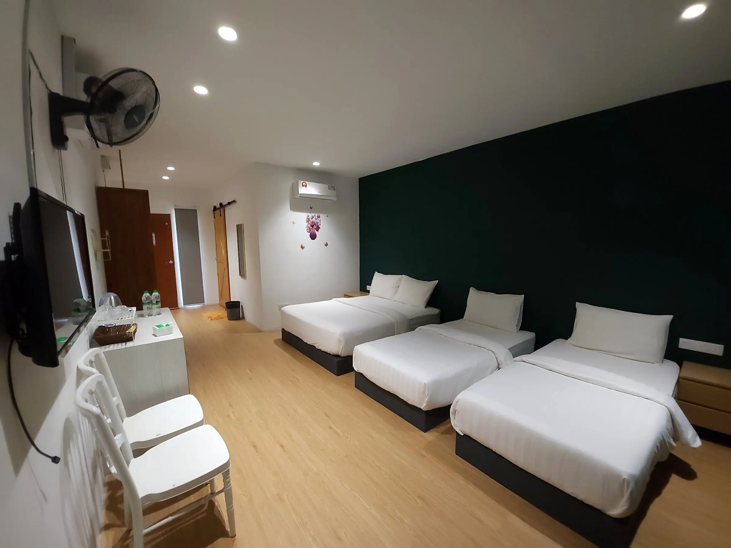 Wide view of a Family Room: three beds, wall TV, chairs and a timber door to the ensuite