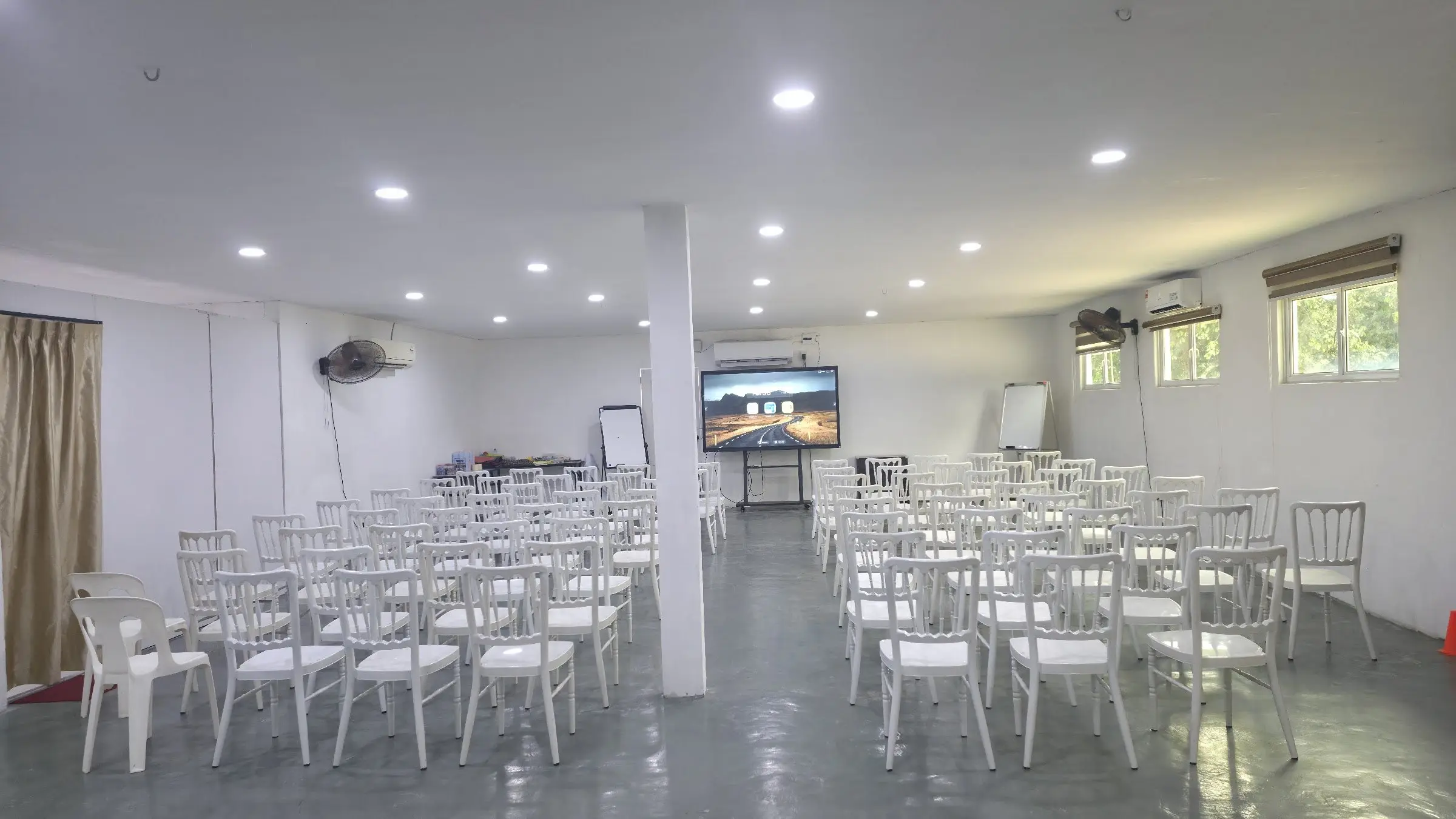 The bright meeting hall set theatre-style, with white chairs facing a large TV screen and flip charts