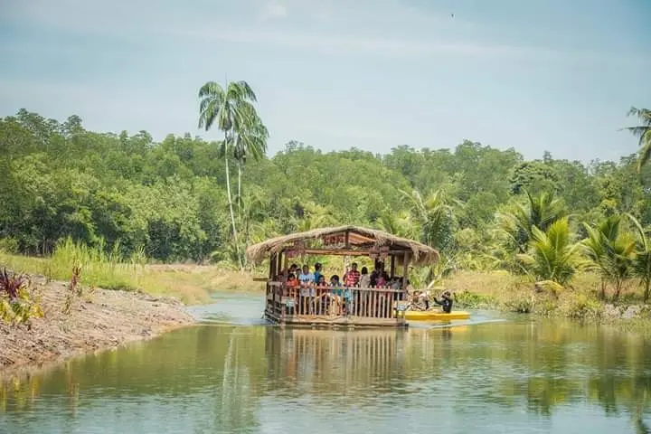 A thatched River Cruise boat with guests on a calm, jungle-lined river